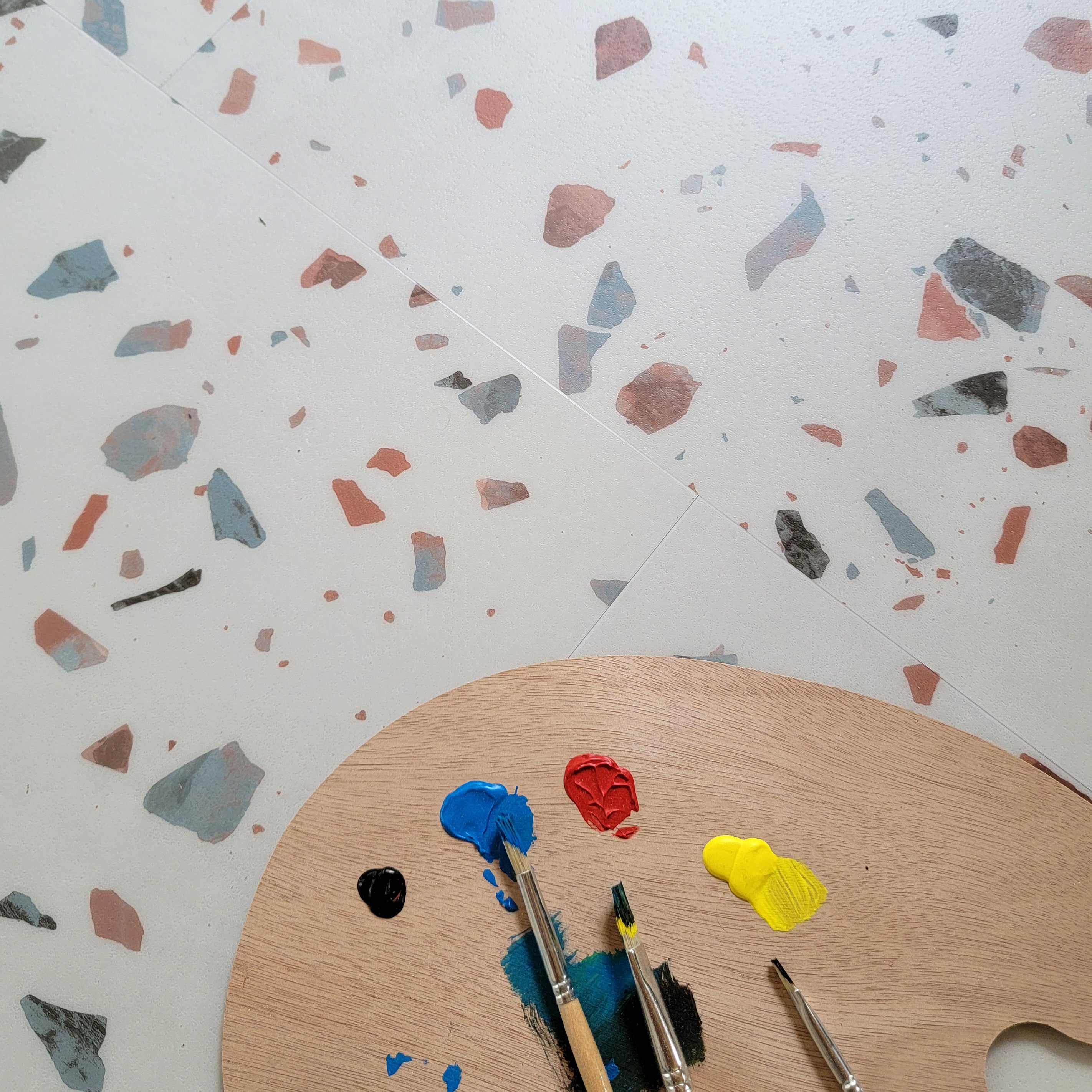 close up of Earl Grey terrazzo vinyl tiles with artists pallet, brushes, and paint