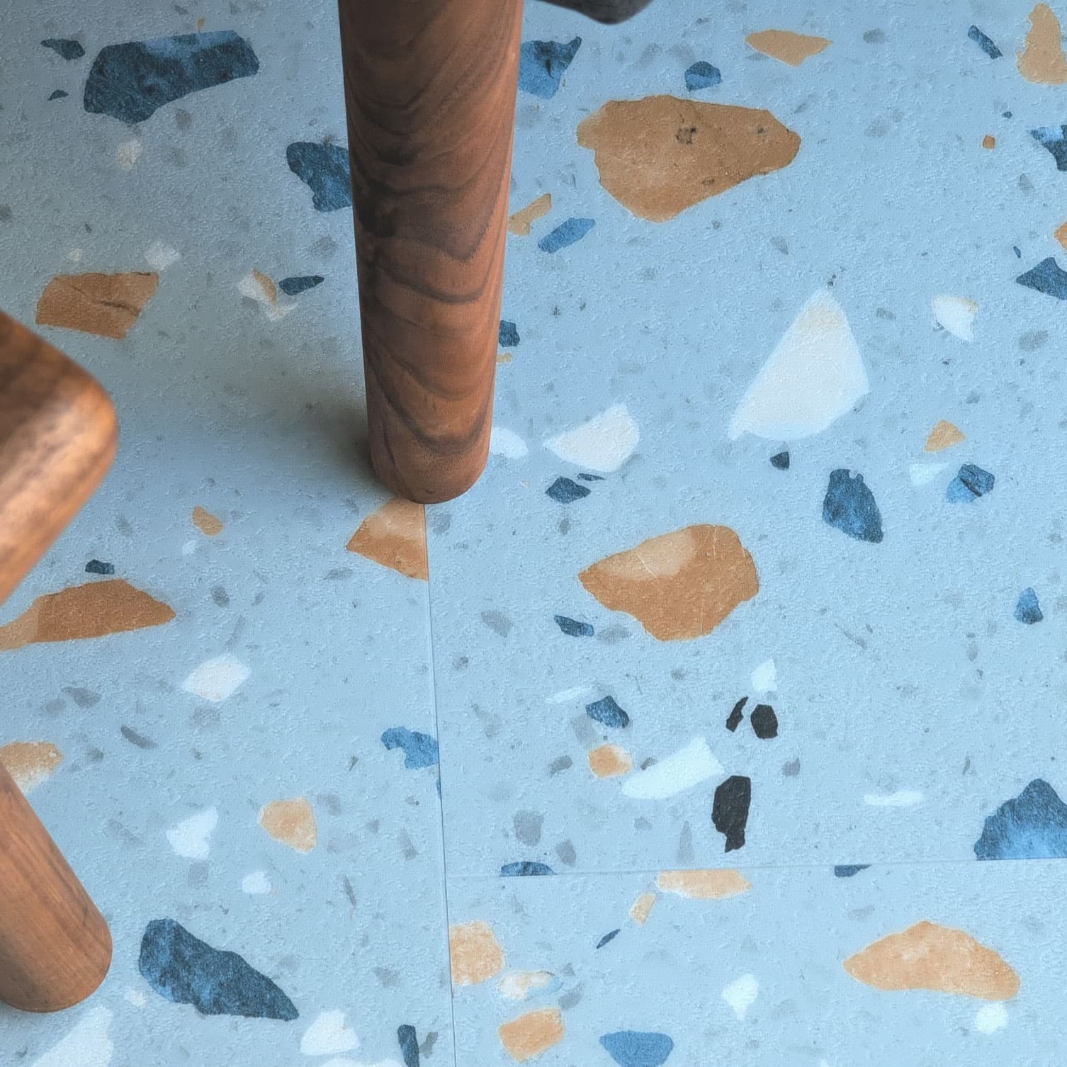 Close up of Allure Blue Agave Terrazzo LVT with furniture leg visible.