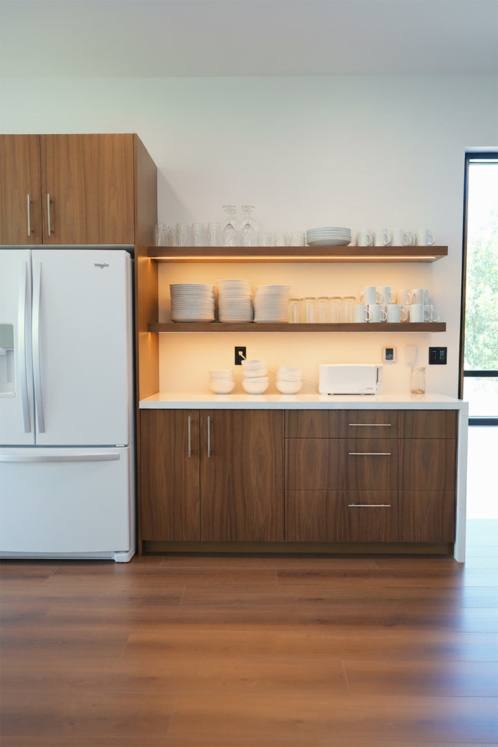 Modern kitchen with wooden cabinets, reddish wood LVP, white appliances, and open shelves.