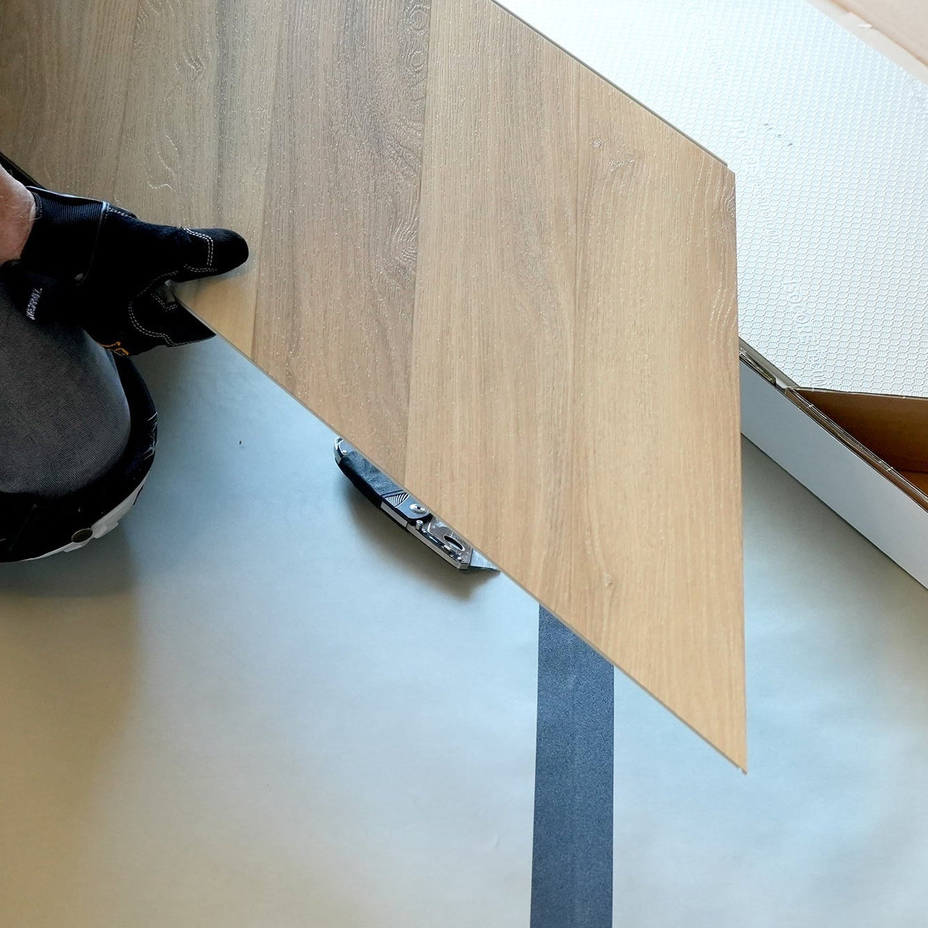 Person holding a chevron flooring piece with a cardboard box on a white floor.