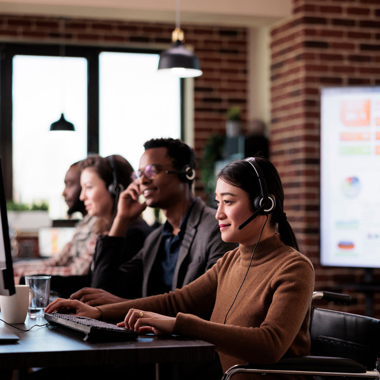 Four customer care representatives with headset on looking at computer screens.