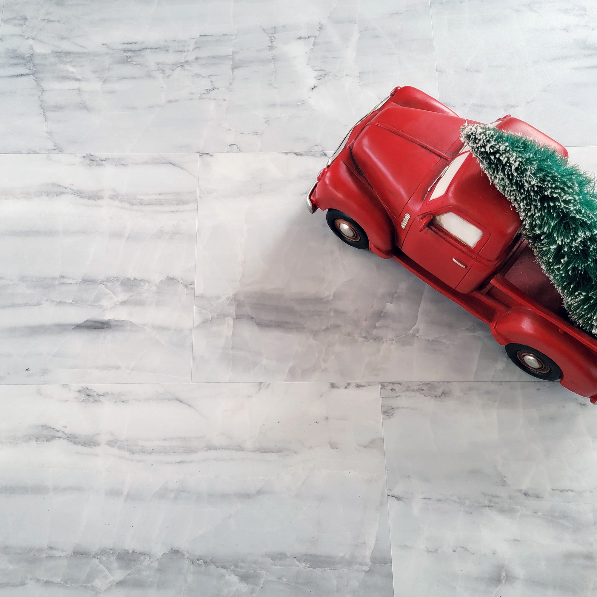 A red toy truck with a Christmas tree on its roof is positioned on europa brulee marble luxury vinyl tile floor.