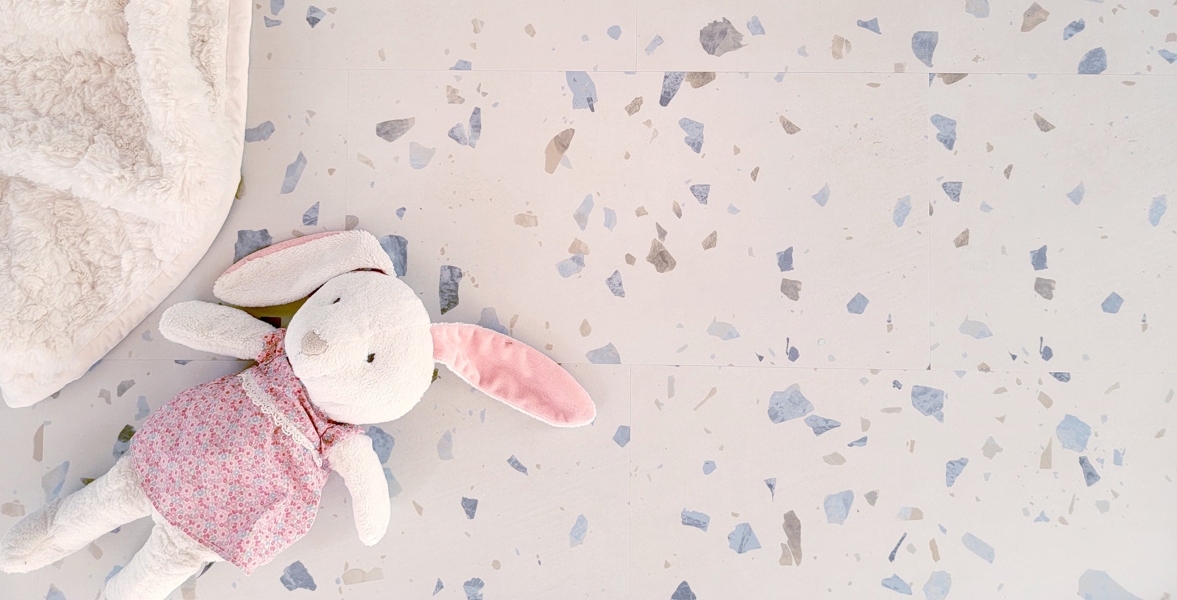Terrazzo vinyl tile flooring with a stuffed rabbit and blanket.