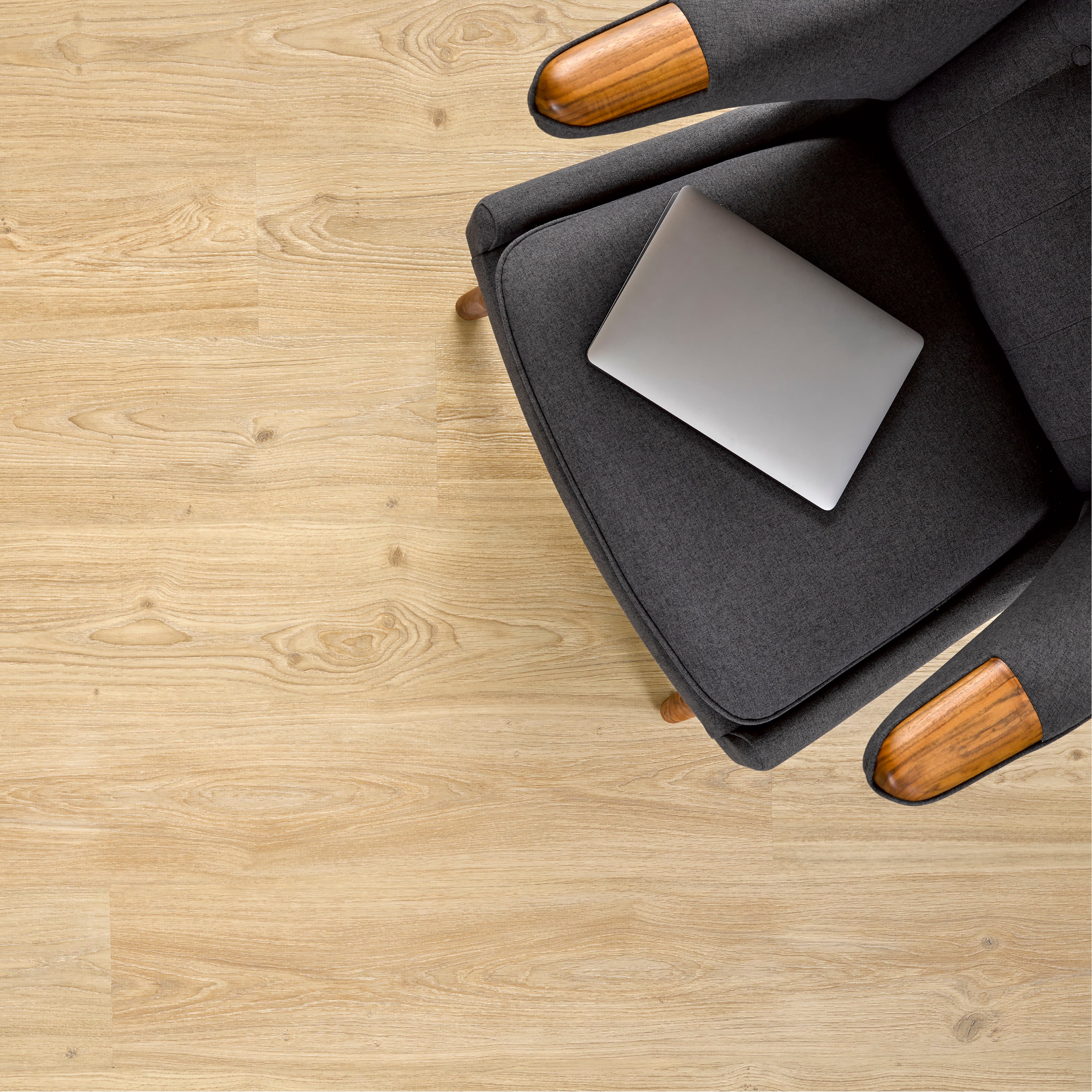 Allure Soft Oak luxury vinyl flooring with dark gray chair with wooden armrests and legs, featuring a silver laptop on a light wood floor.