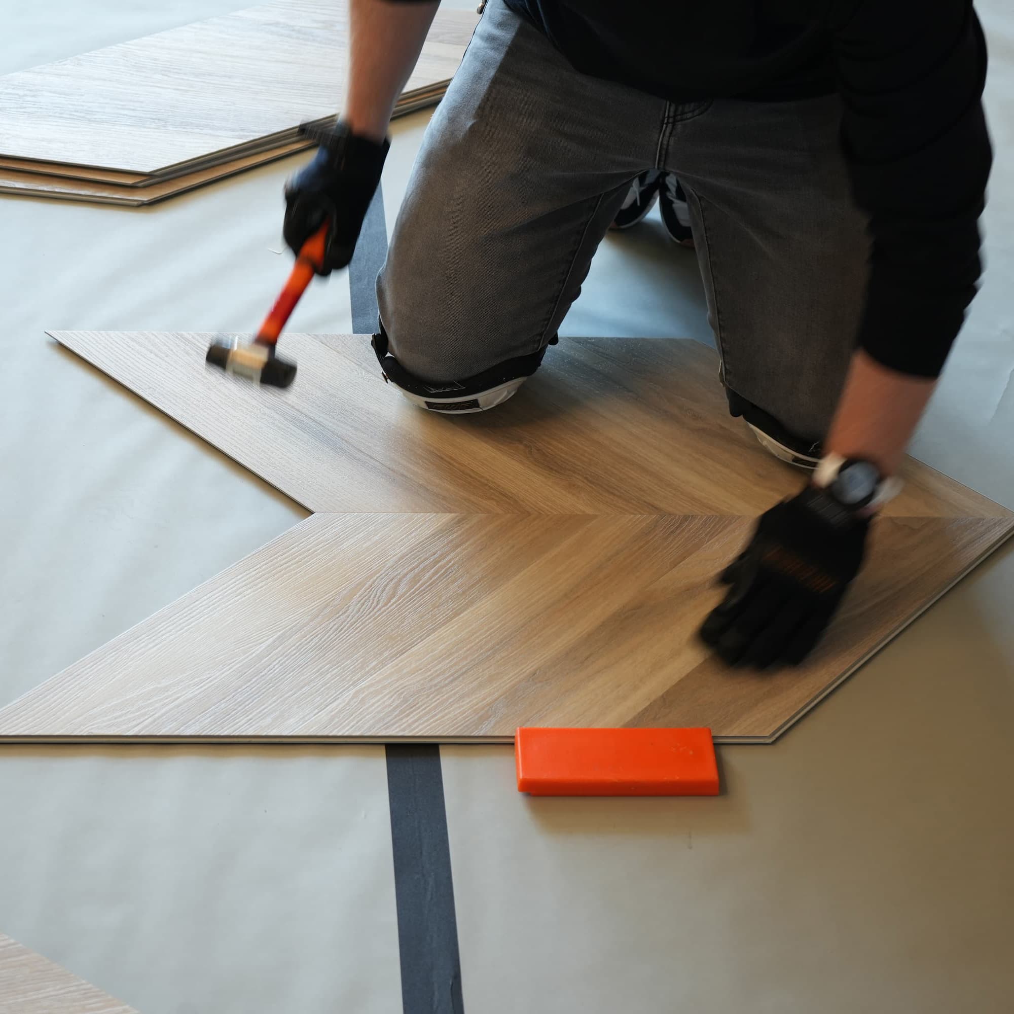 man installing light wood chevron design vinyl flooring by Allure