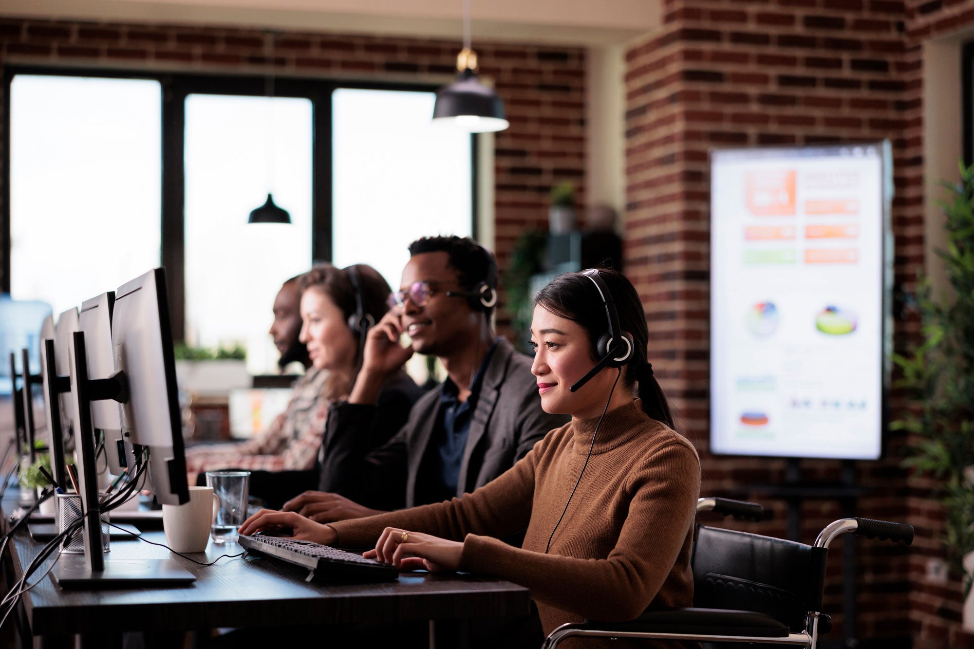 Four customer care representatives with headset on looking at computer screens.