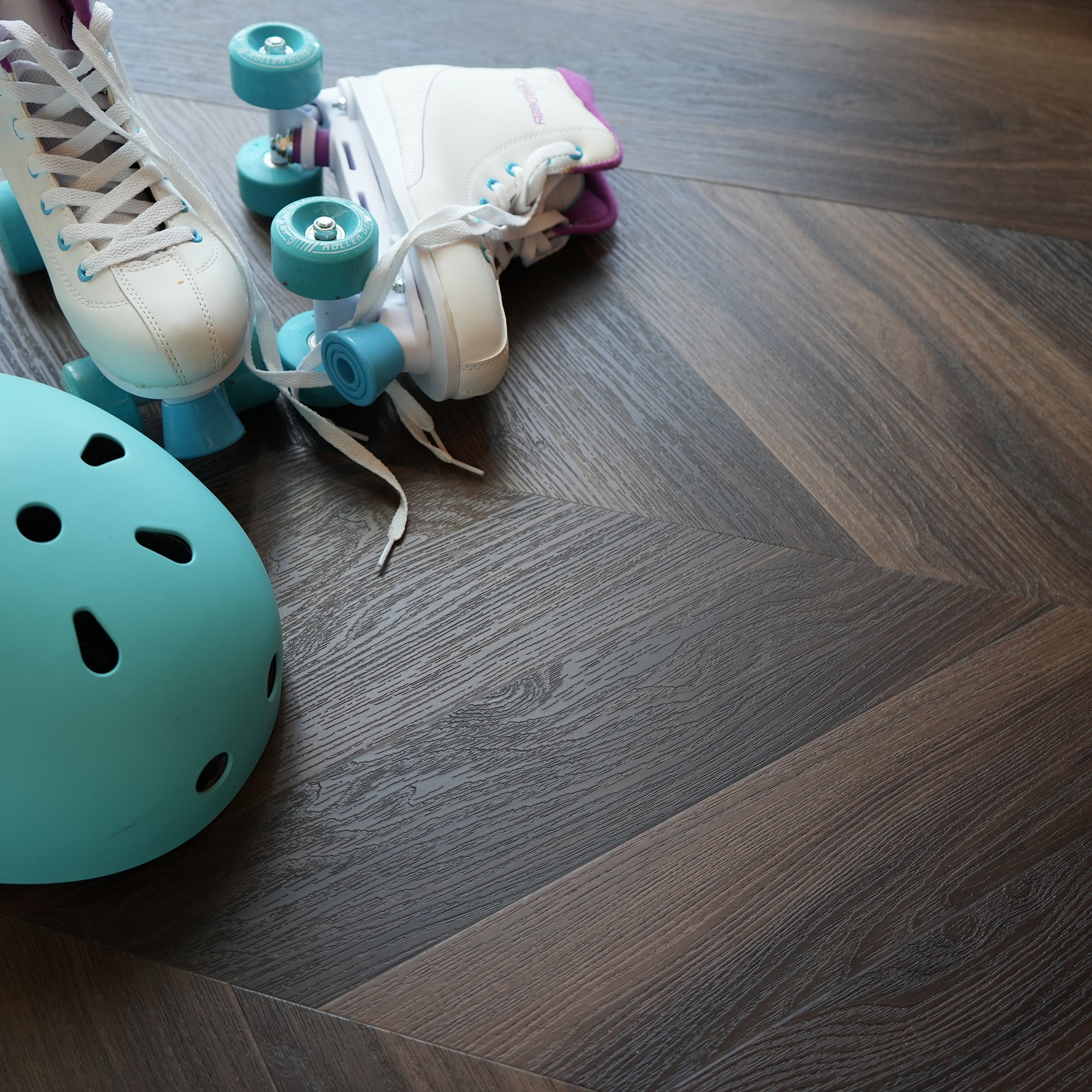 Roller skates with turquoise wheels and a teal helmet on a dark wood look chevron vinyl floor