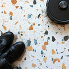 Black combat boots and a robot vacuum cleaner on a honeydew terrazzo vinyl tile floor.