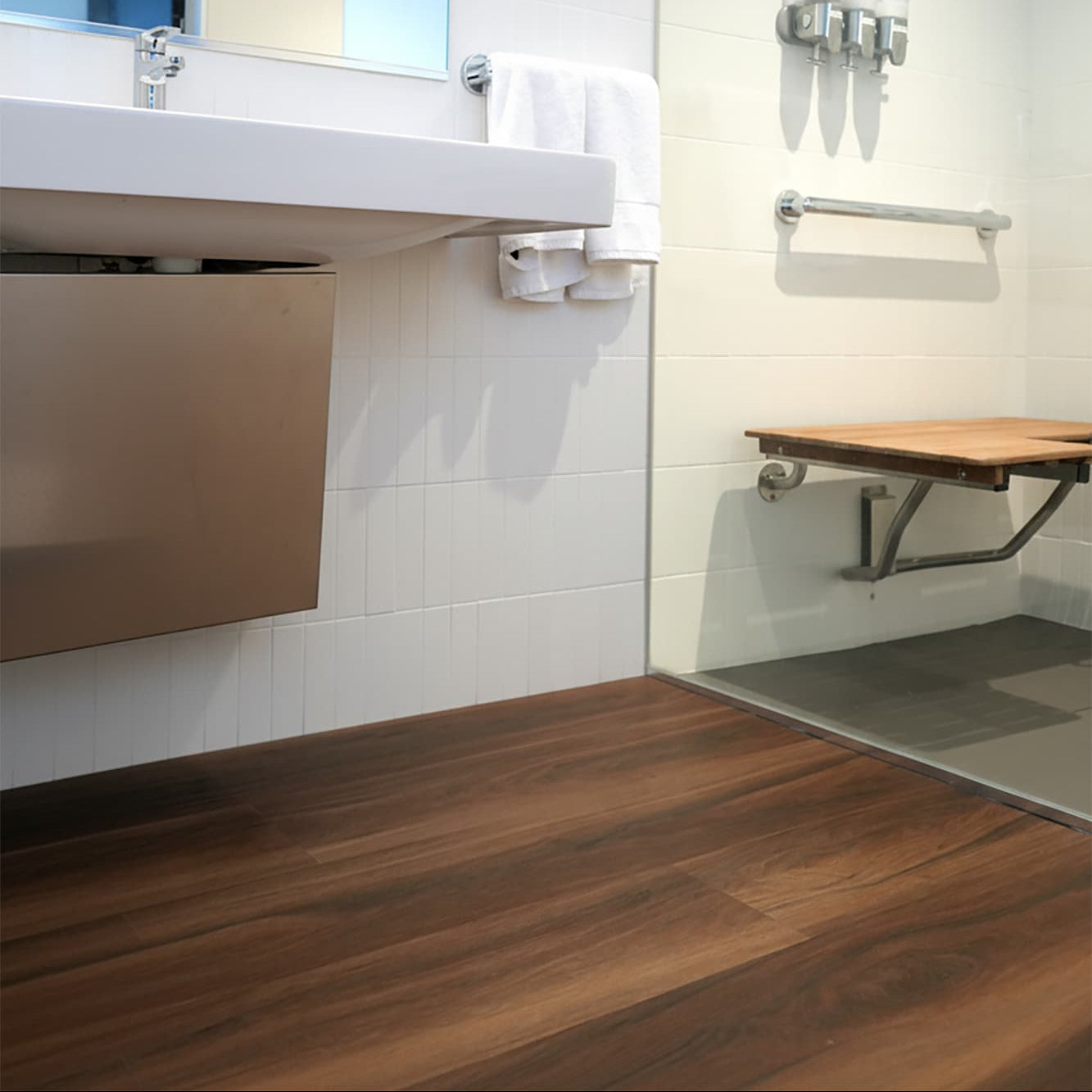Modern commercial bathroom with Allure reddish wood LVP floor, mirror, towel rack and shower stall.