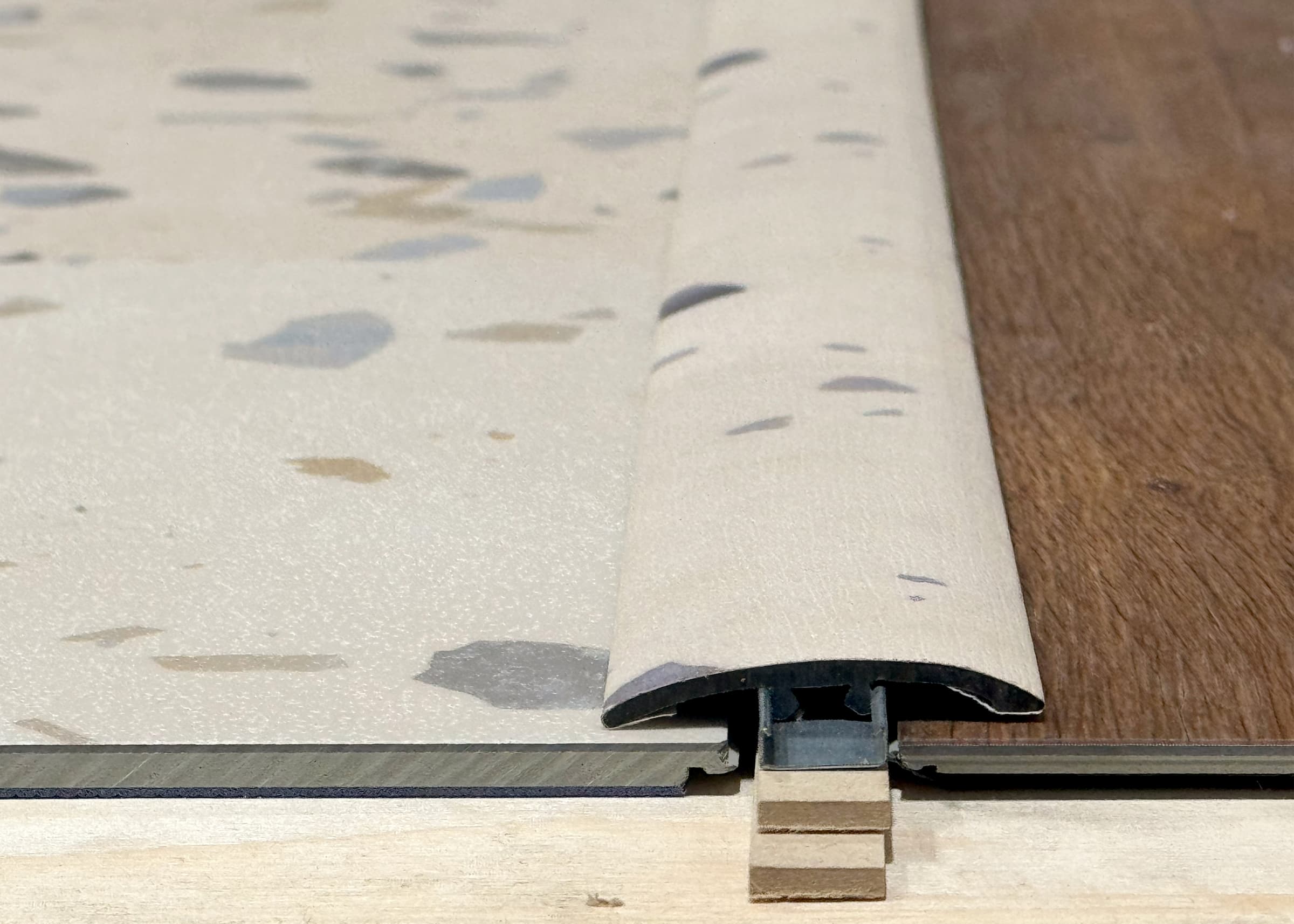 Close-up of a T molding and reducer trim on a terrazzo LVT and LVP floor transition strip.
