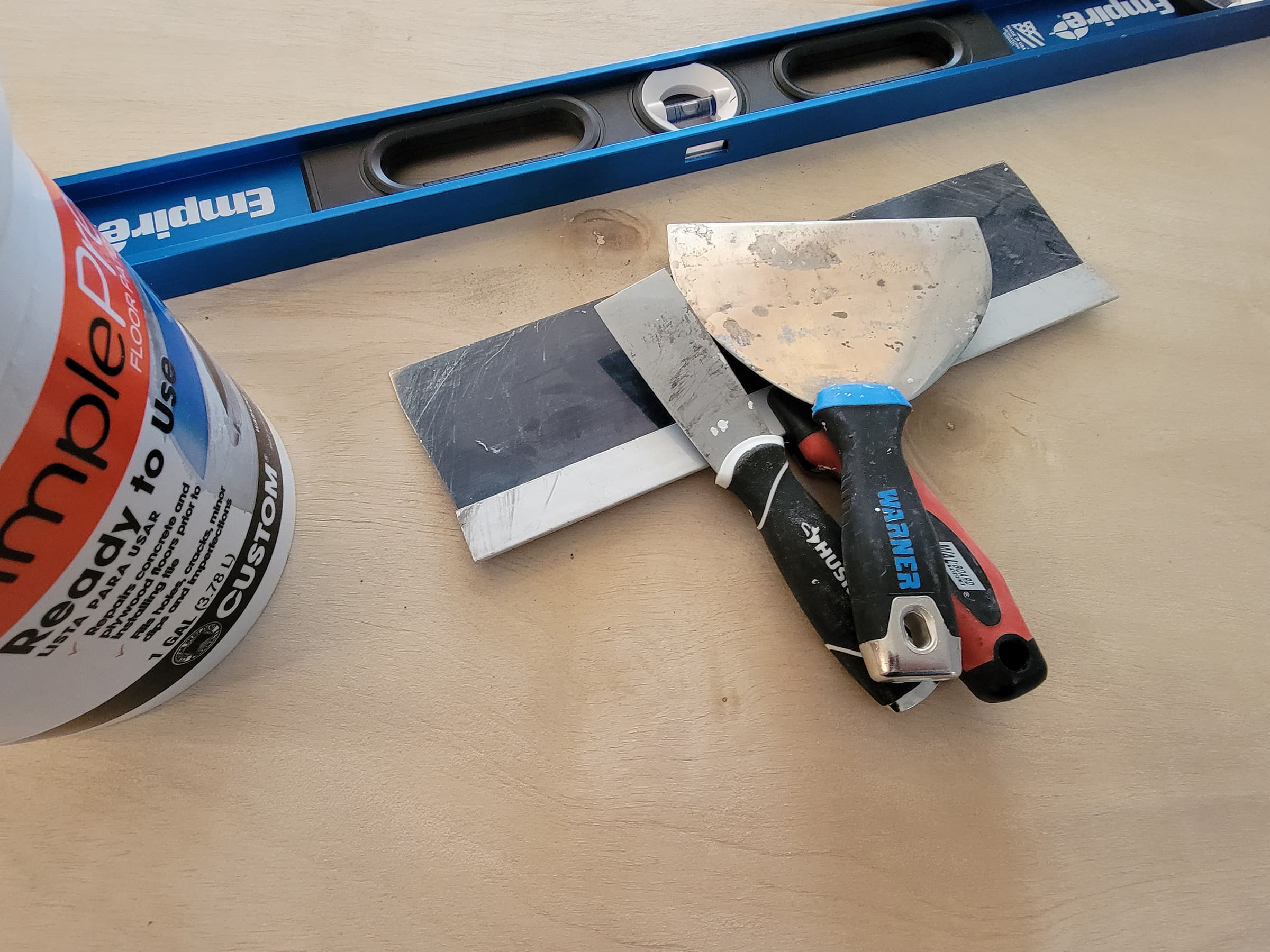 Floor patch, scrapers and a large bubble level on a plywood floor