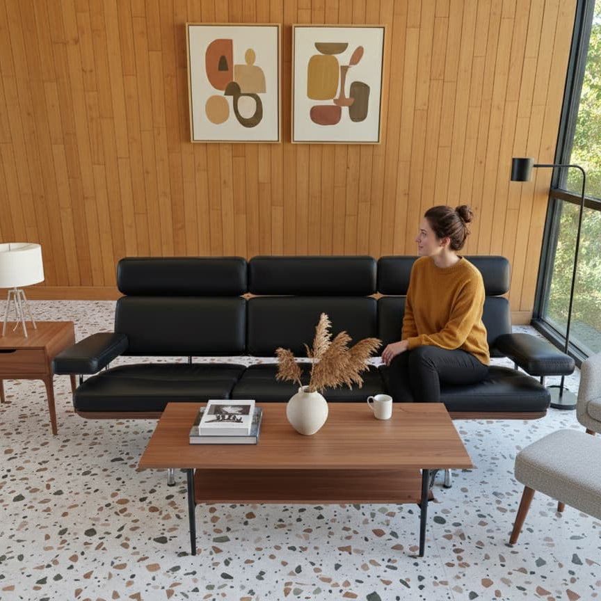 Woman sitting on a black sofa in a modern living room with wooden walls and terrazzo vinyl tile flooring.