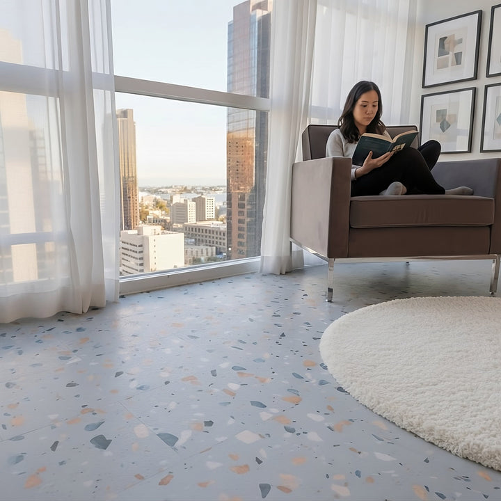 Woman sitting in modern chair reading in condo with Blue Agave Terrazzo vinyl tiles by Allure